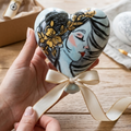 Cuore a forma di palloncino in ceramica azzurro polvere con nastro in raso, decorato a mano con il profilo di una ragazza a matita e dettagli in oro lucido."